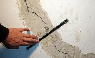 A wall with a large crack is being inspected by a professional in Oakland, CA